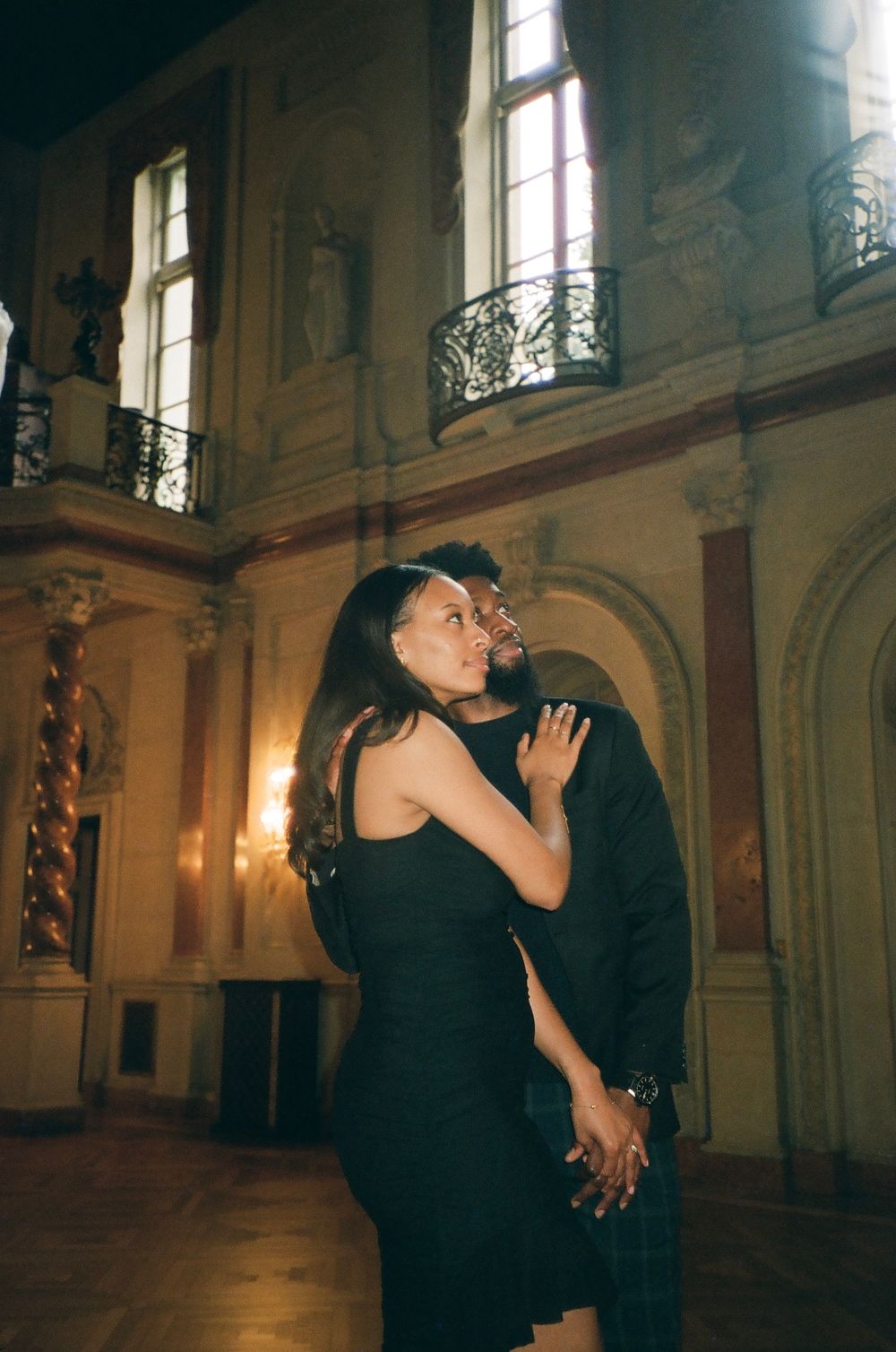 A couple shares an intimate dance moment in a historic building with tall windows and ornate details.