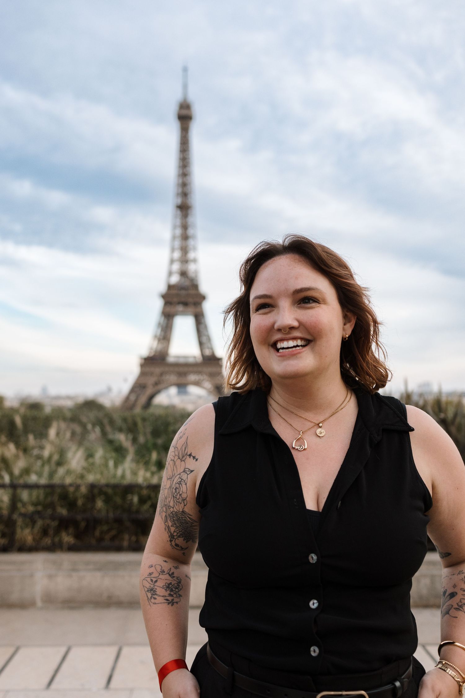 A person in a black sleeveless top poses in front of the Eiffel Tower on a cloudy day in Paris.