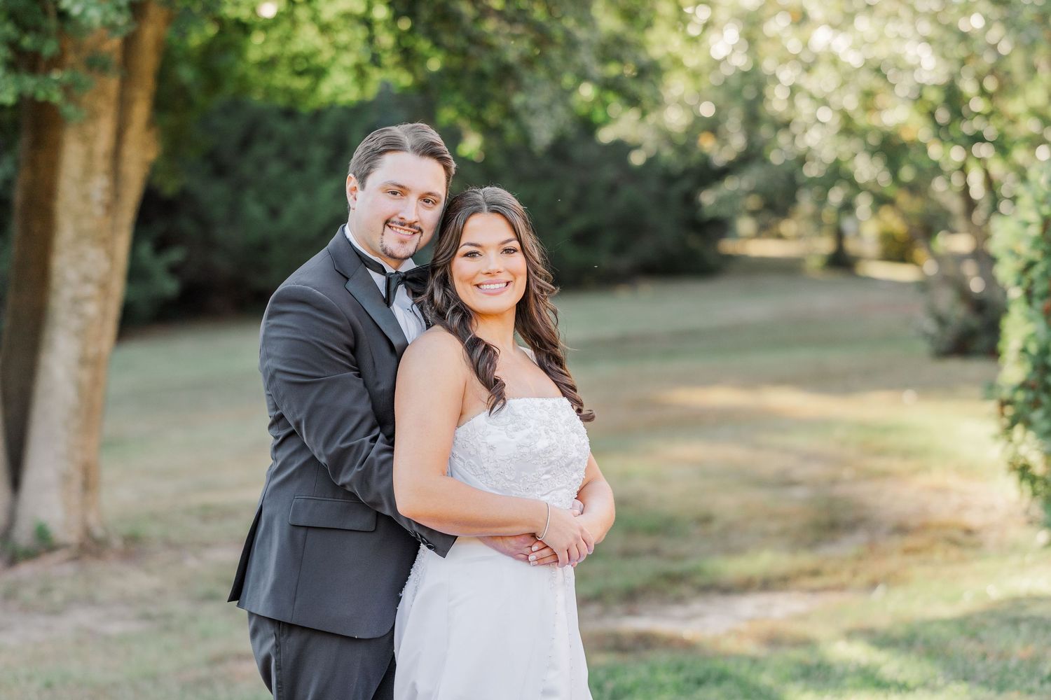 A couple in wedding attire embraces while standing in a sunlit garden setting during their outdoor celebration.