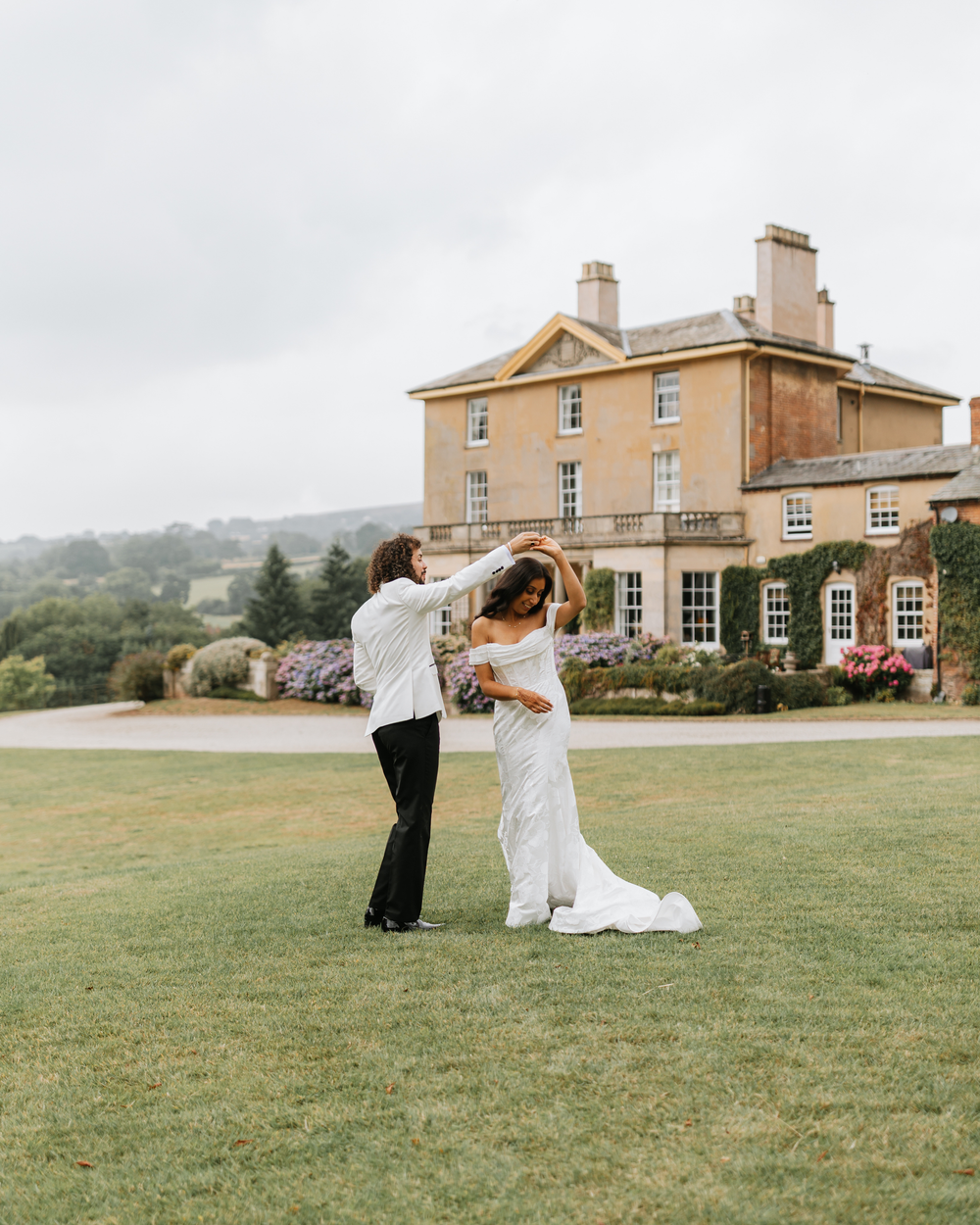 Couple dancing and twirling on a lush green lawn in front of an elegant Georgian mansion on their wedding day.
