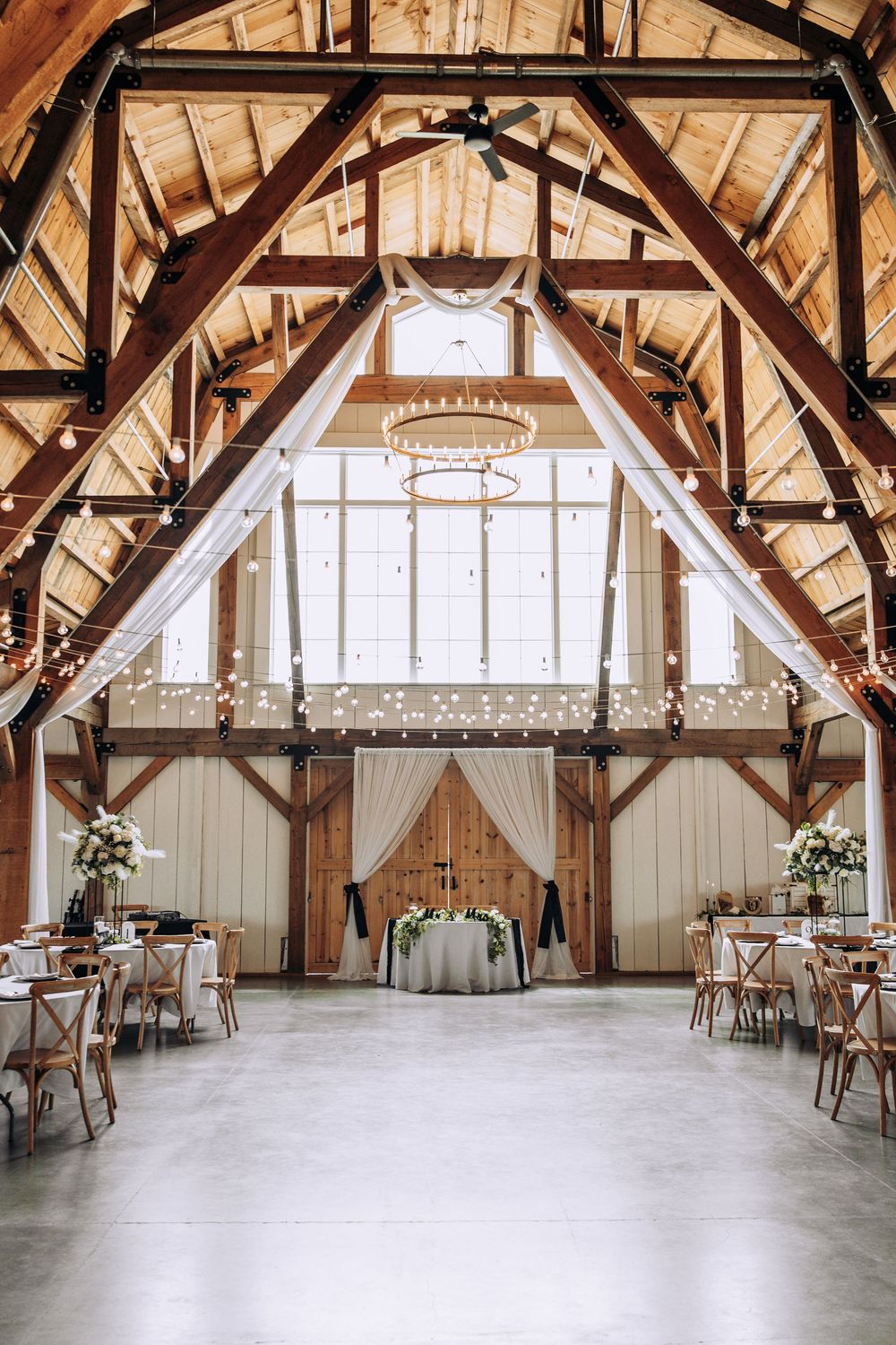Elegant barn wedding reception hall with draped fabric, chandeliers, and sweetheart table.