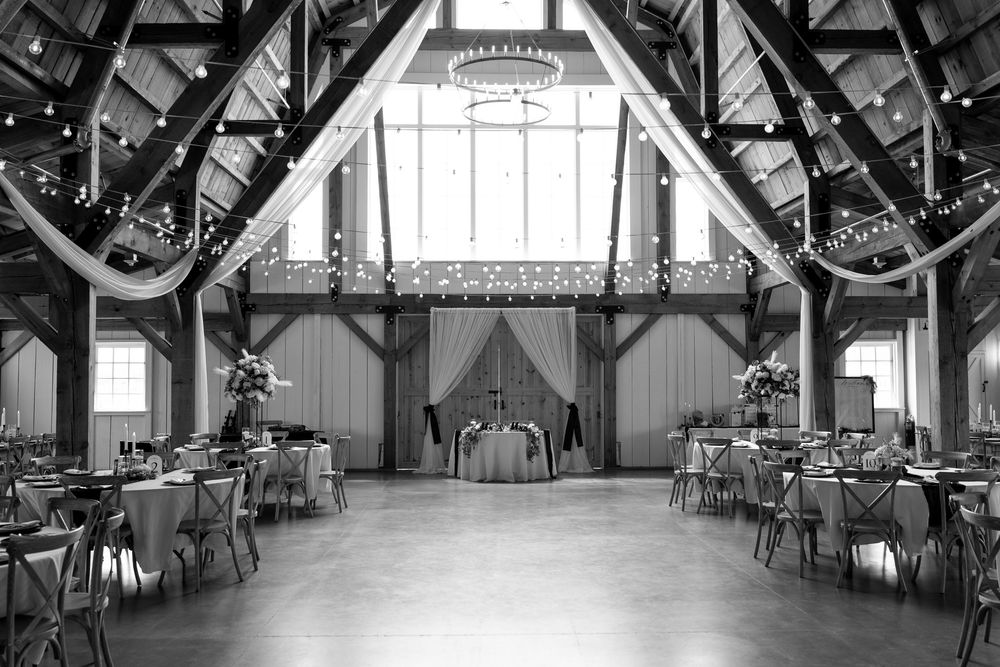 Black and white barn wedding reception with wooden beams and draped fabric decor.