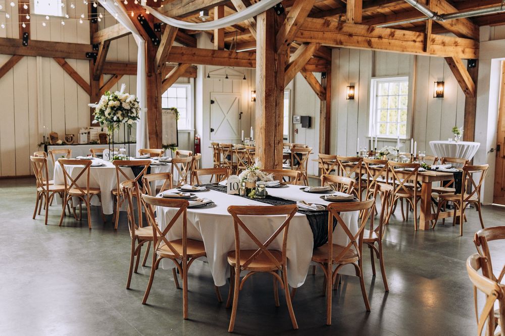 Rustic barn wedding reception with round tables, cross-back chairs, and floral centerpieces.