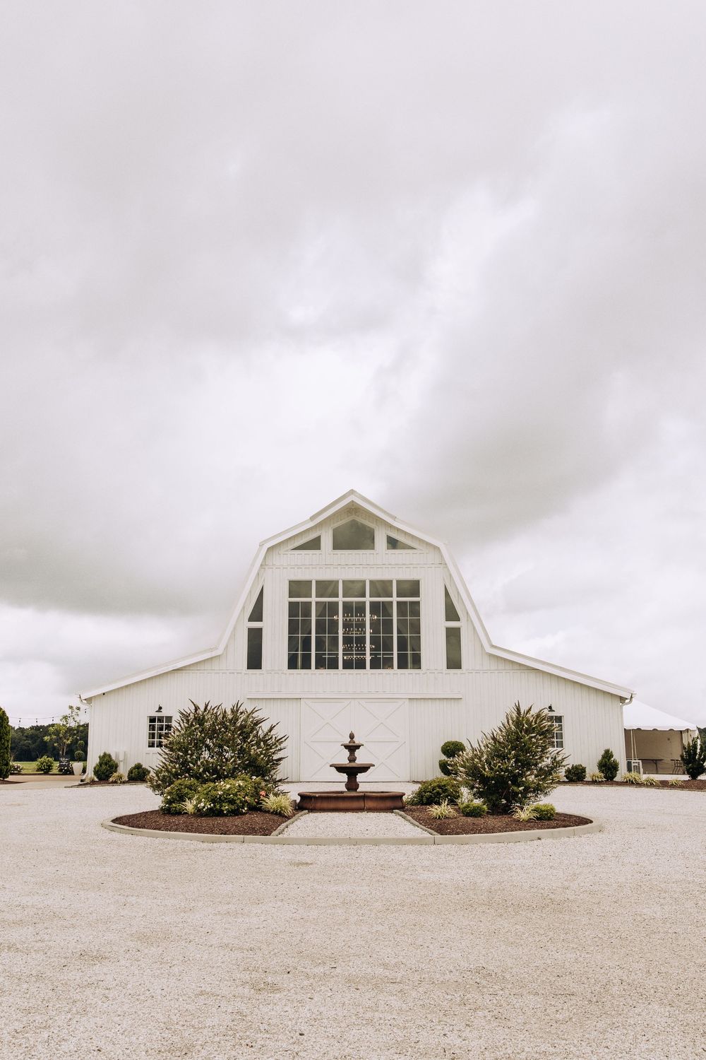 White barn wedding venue with large arched window and small fountain outside.