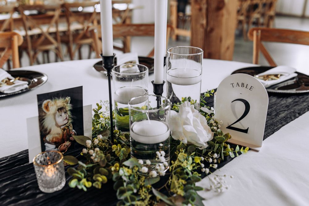 Elegant wedding centerpiece with white florals, greenery garland, black taper candles, and a Table 2 number sign.