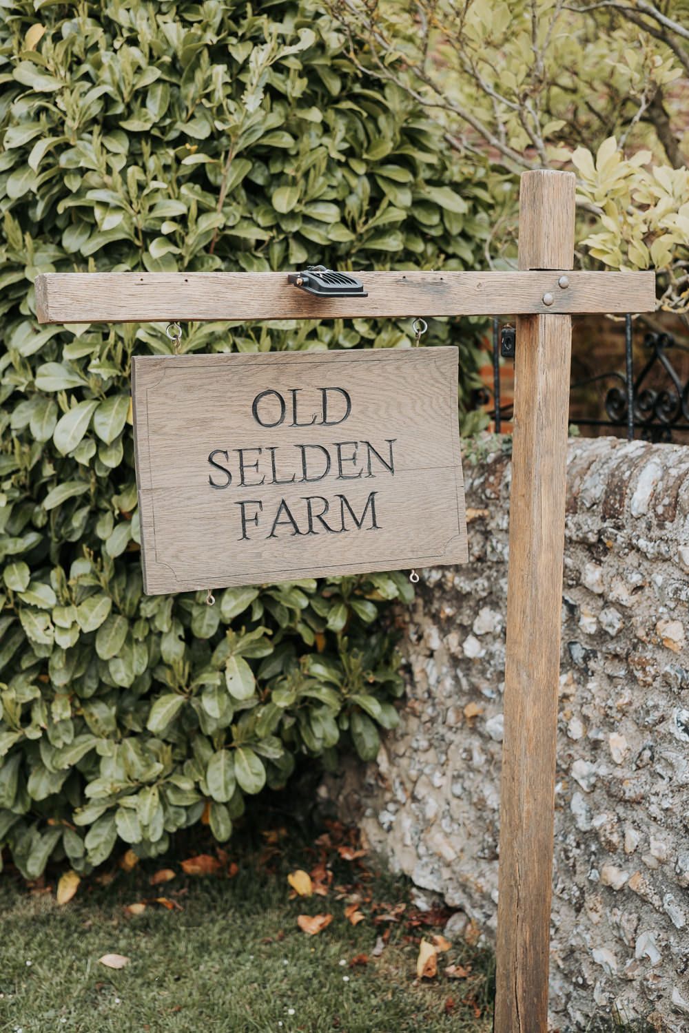 Three rustic wooden signs mounted on posts spell out 'OLD SELDEN FARM' against a stone wall and green foliage background.
