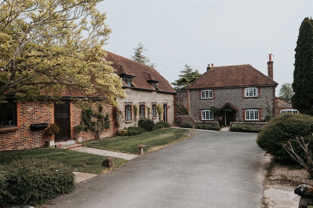 A series of rustic brick buildings and homes line a winding country road in a rural English setting.