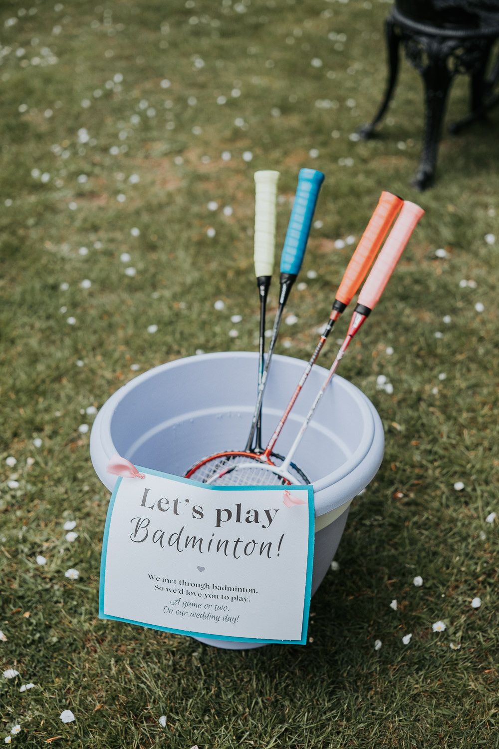 Blue plastic dish with badminton shuttlecocks and racquets on grass with a 'Let's play badminton' sign.