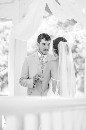 Black and white wedding portrait captured through flowing white fabric in an outdoor setting.