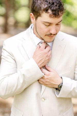 Close-up of someone adjusting their tie while wearing a cream-colored suit jacket.