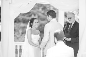 A wedding ceremony takes place under a white gazebo with guests watching.