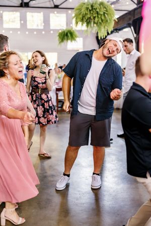 Wedding party dances energetically at a reception with string lights overhead.