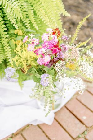 Delicate floral centerpiece with ferns and pink blooms on wooden surface.