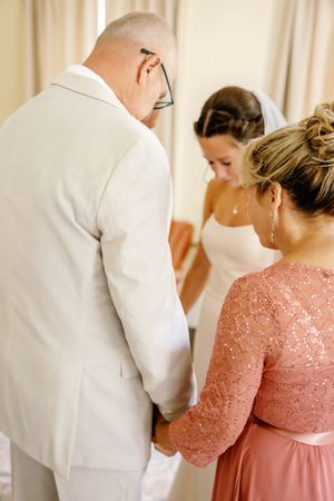 A person in a white suit and another in a pink dress stand together during a wedding preparation moment.