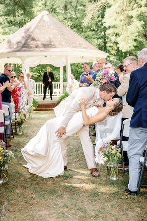 A romantic dip kiss during an outdoor wedding ceremony under a gazebo.