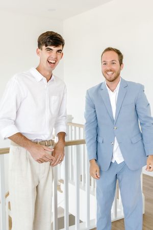 Two people in formal attire sharing a laugh by white stair railing.