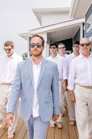 Wedding party in light blue suit and white shirts posing on beach house deck.