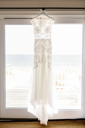 Elegant lace wedding dress hanging in window with ocean view.
