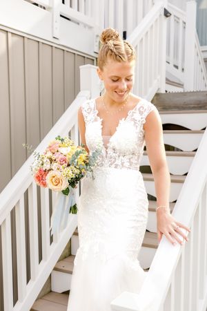 A bride holds bouquet while descending white outdoor stairs.