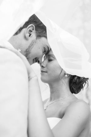 Intimate black and white portrait of newlyweds sharing a tender moment under a veil.