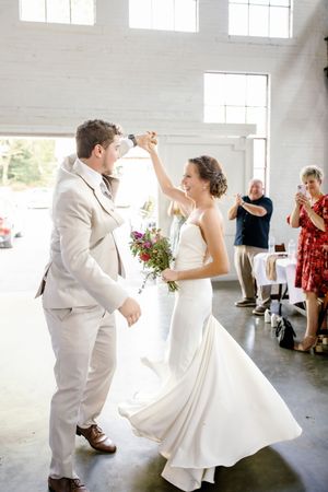 A couple dances and celebrates during their first dance at a bright indoor wedding reception.