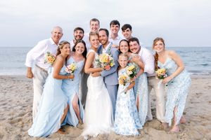 Wedding party poses together on beach in light blue and white attire.