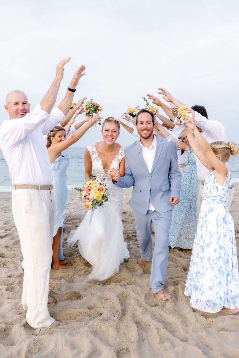 Joyful wedding party jumps and celebrates on sandy beach.