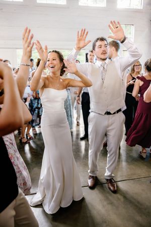Wedding guests dance with hands raised during a lively reception celebration.