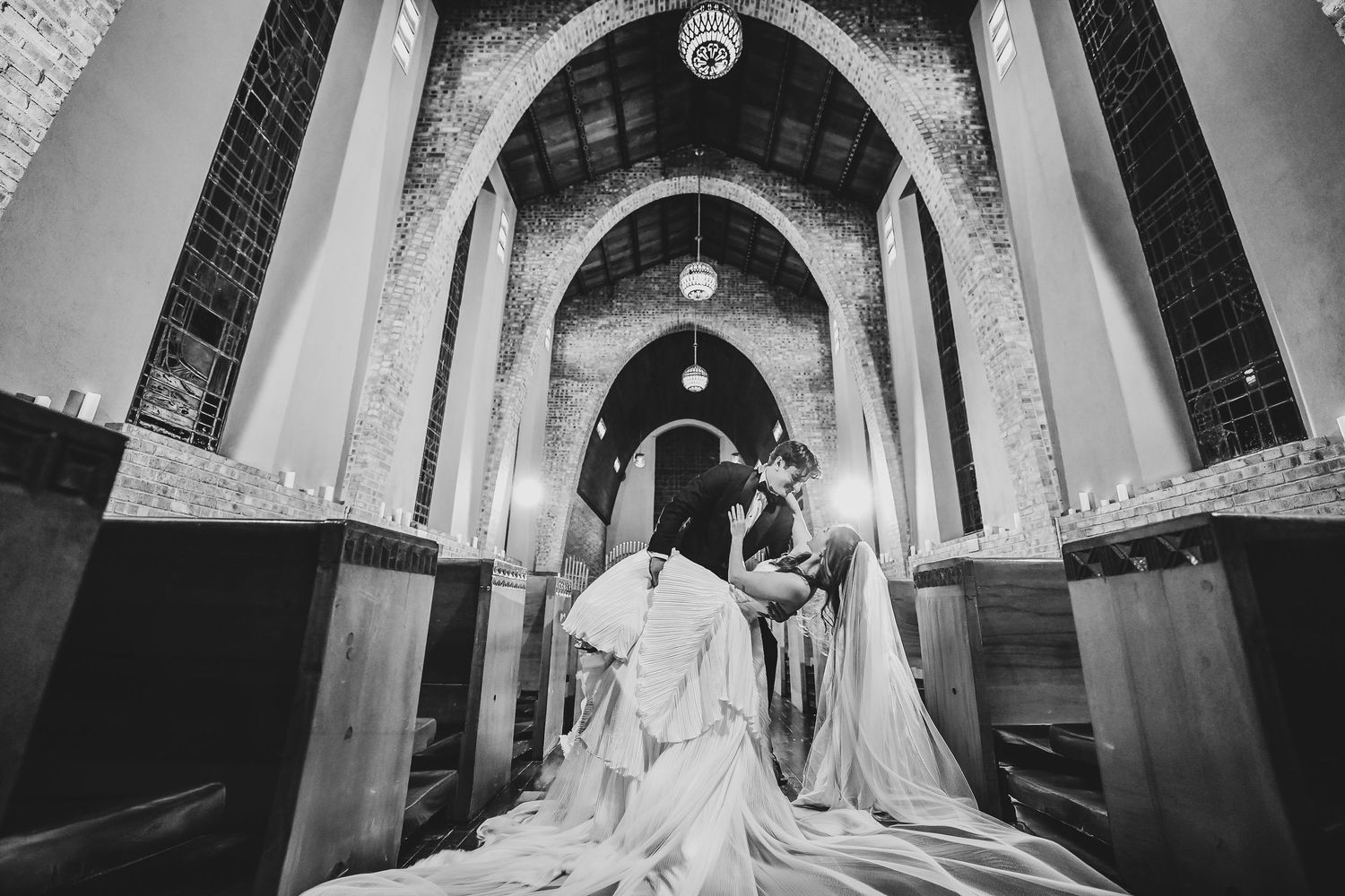a groom dips his bride into a dramatic kiss down the aisle of the little chapel in the woods in denton
