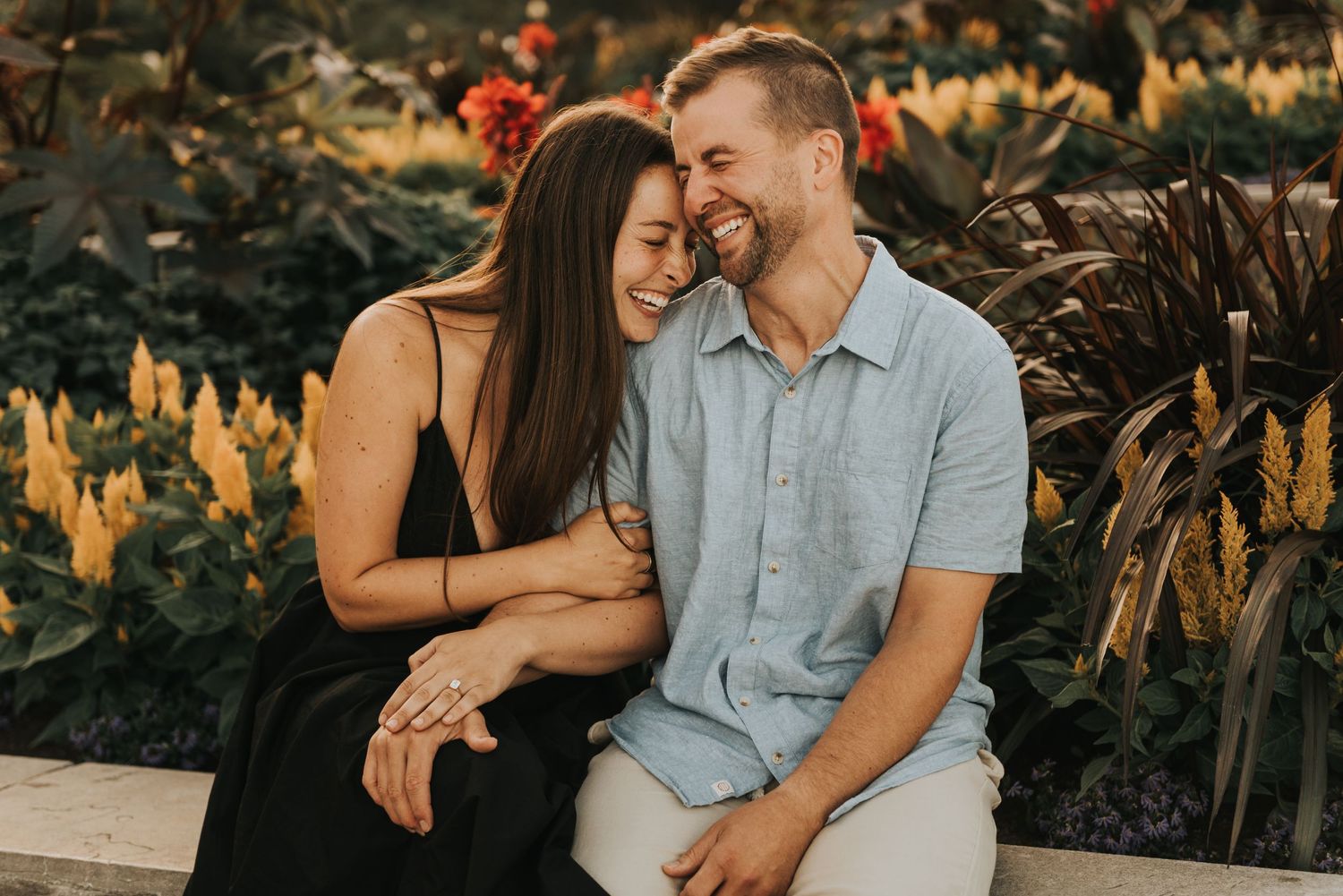 A couple shares an intimate moment while sitting together at sunset in a garden with golden foliage.