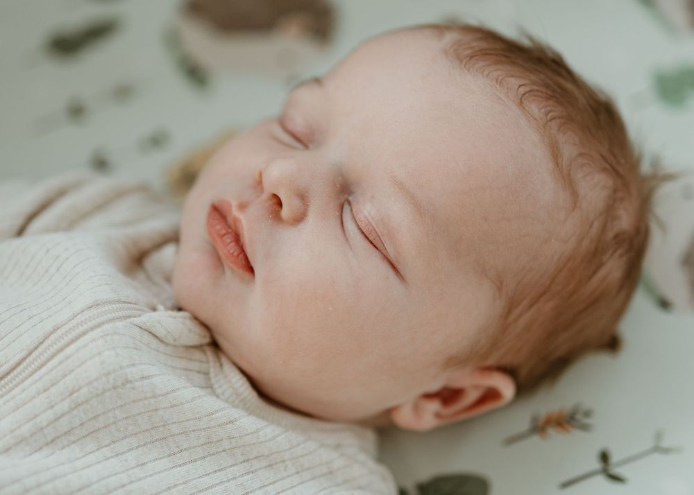 A peaceful sleeping baby wearing a cream colored sweater rests on floral patterned bedding.