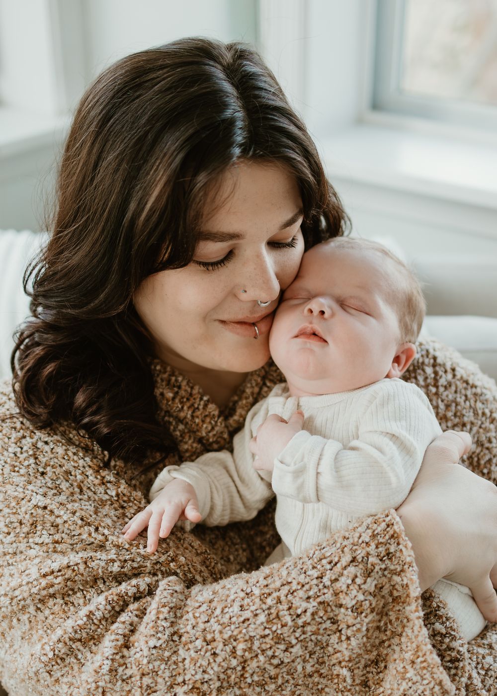 Parent and baby sharing tender moments together on a cozy knit blanket in soft natural light by a window.