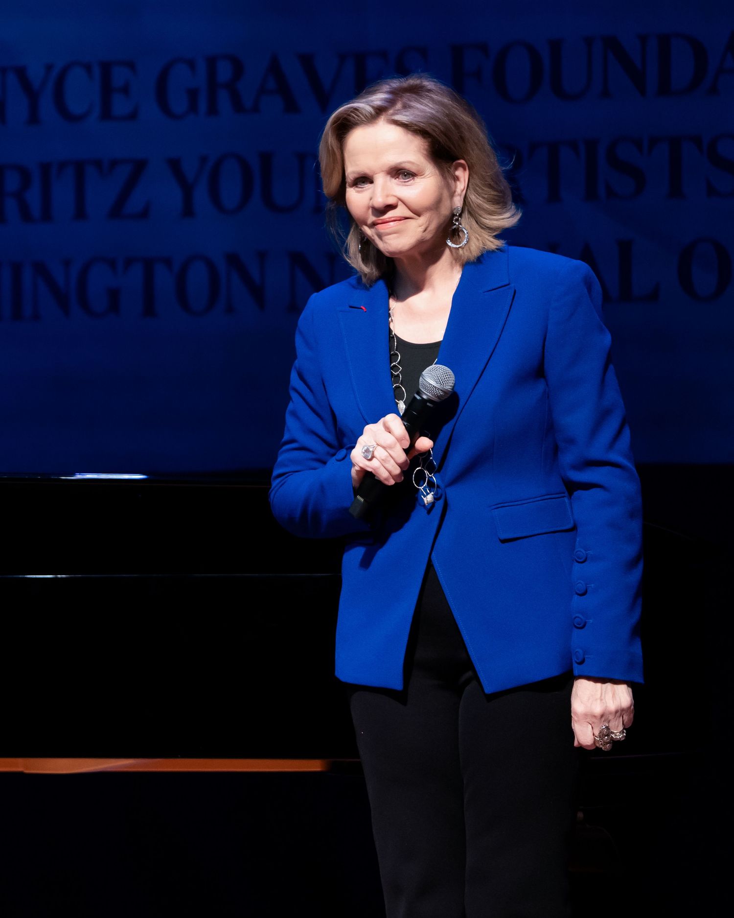 Performer in bright blue blazer speaks into microphone during stage show.