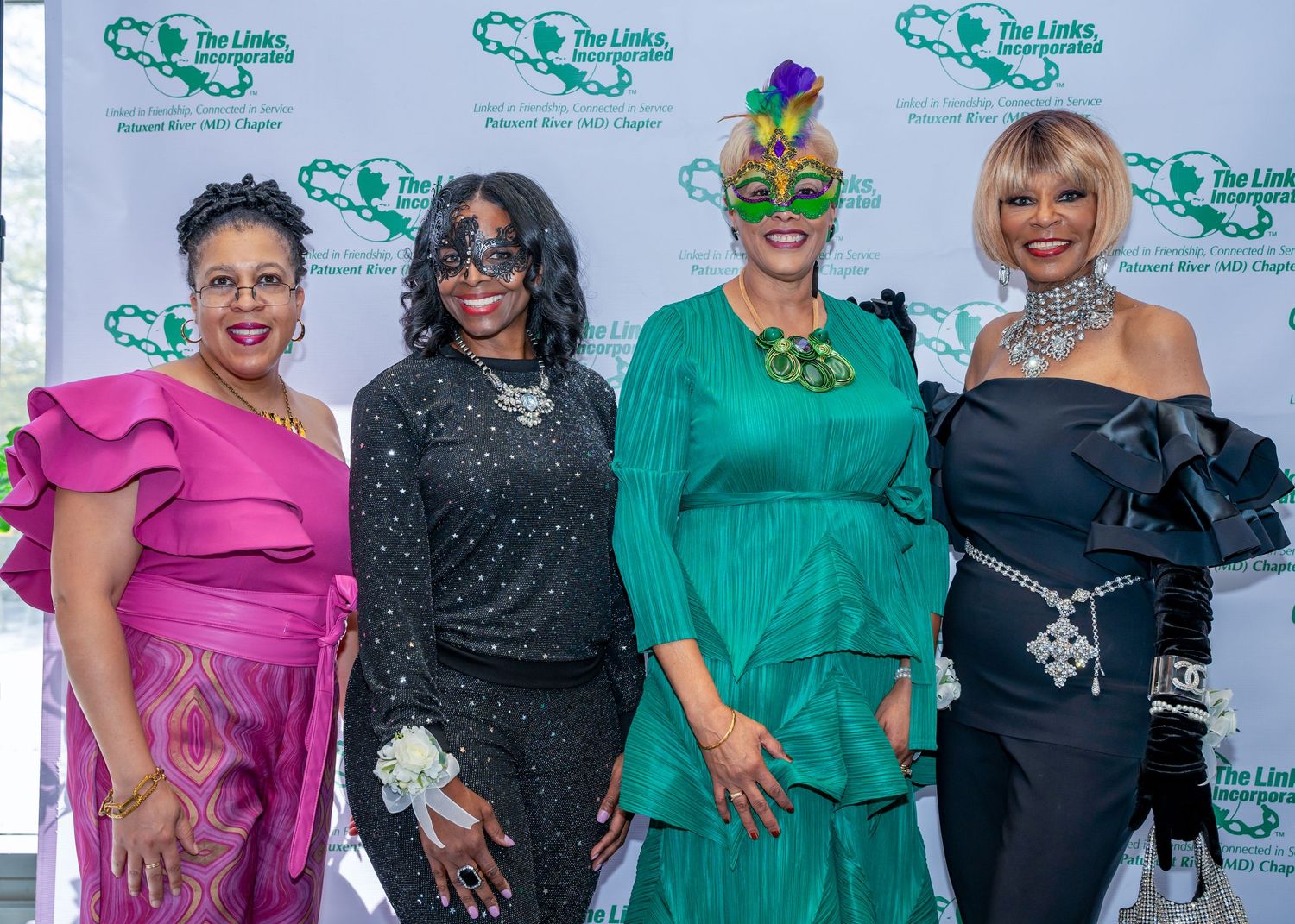 Four attendees in vibrant formal attire pose at a charity event with decorative masks.