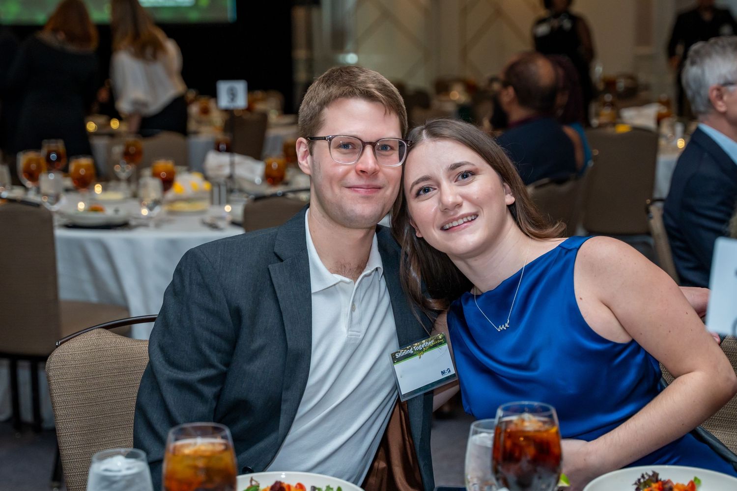 Couple in business casual attire seated at dining table with iced beverages.