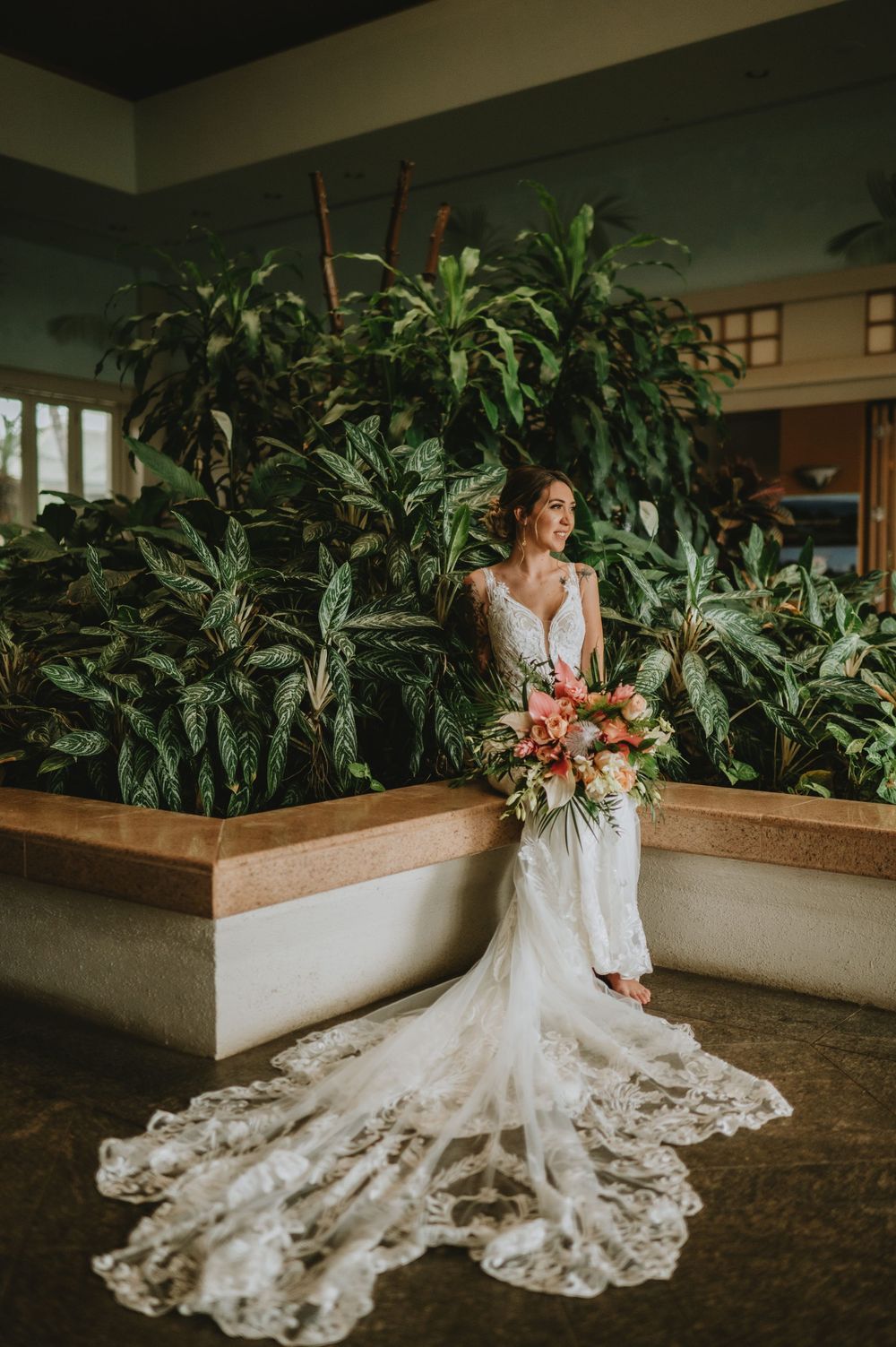 A stunning bridal portrait featuring a lace mermaid wedding dress and tropical indoor garden backdrop.