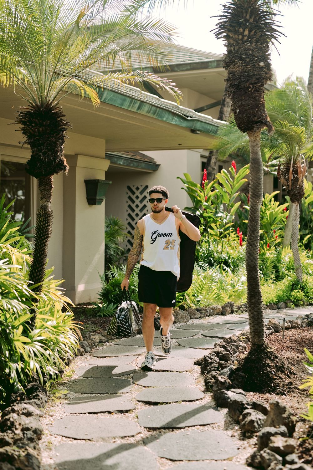 A person walks along a curved garden path lined with tropical palm trees and lush greenery at a resort.