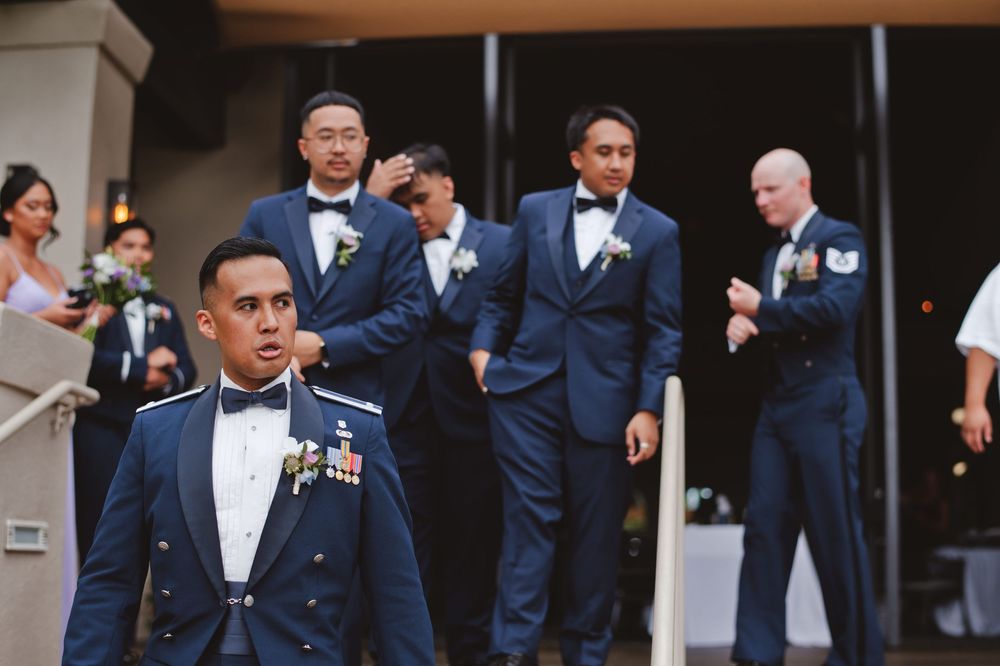 A group of men in formal navy suits and bow ties stand together at a formal event.