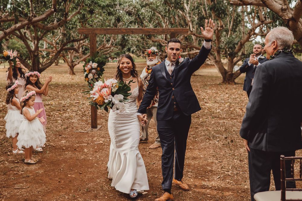 Romantic wedding couple embraces under rustic trees in an outdoor garden setting.