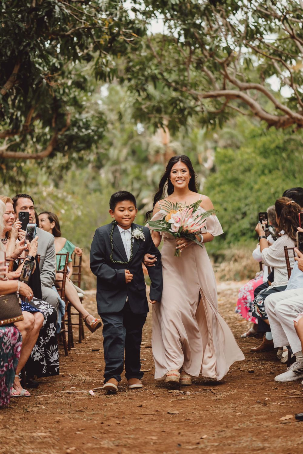 Wedding guests crouch down to take photos during an outdoor ceremony.