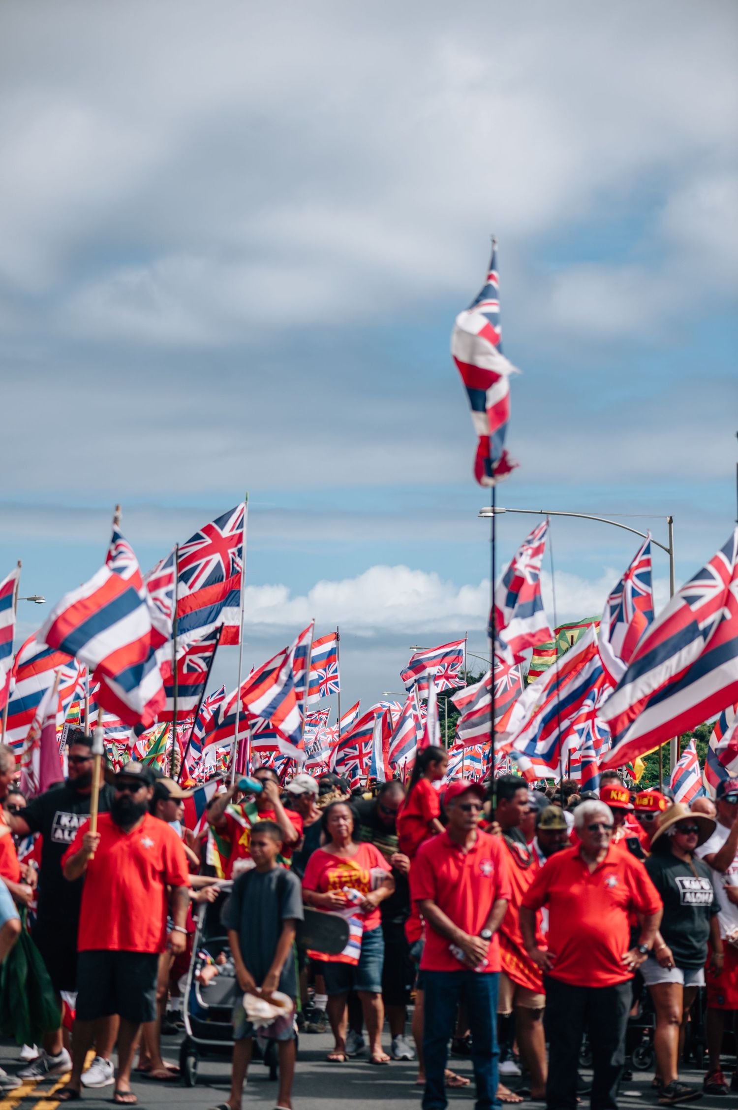 Demonstrators in red shirts wave Hawaiian flags during a public gathering.