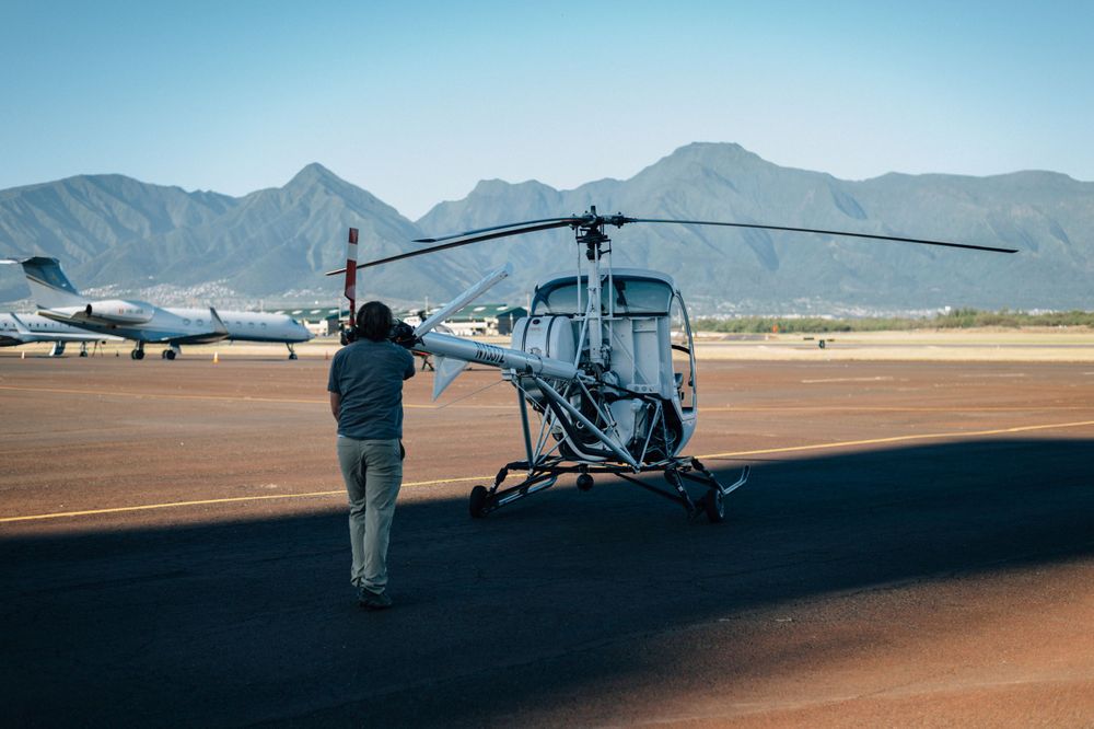 Helicopter and ground crew on desert airfield with mountain range in background.