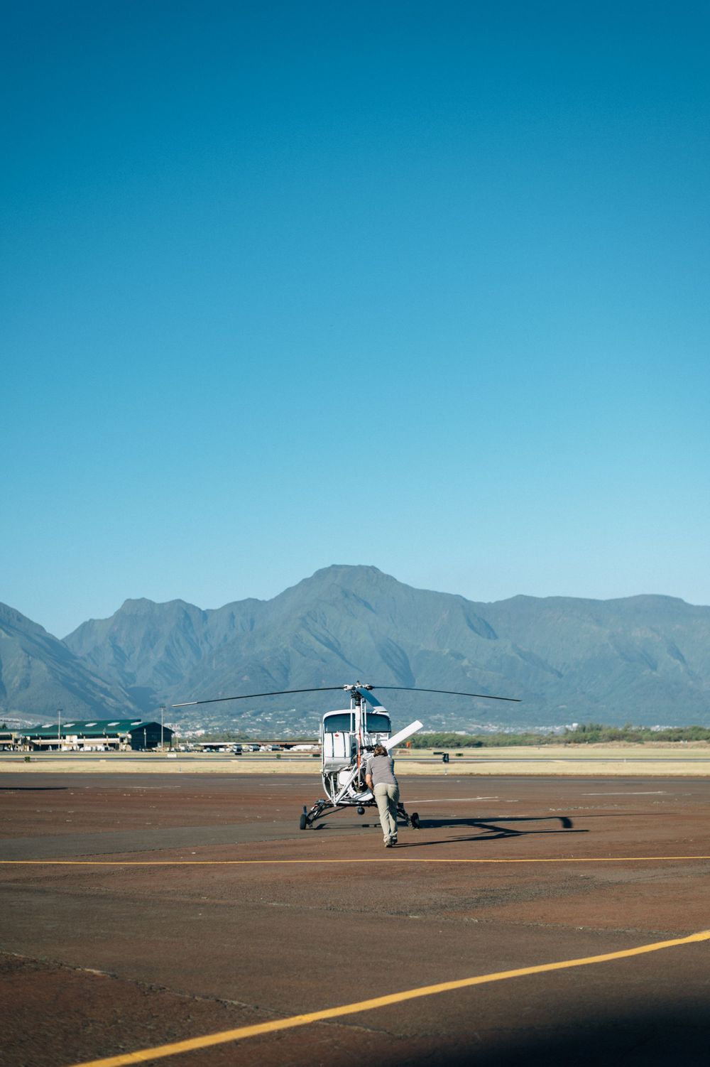 Helicopter stationed on desert airstrip with mountain range visible in distance.