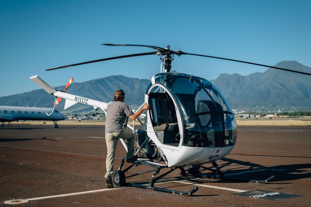 White helicopter parked on airfield with mountains visible in background.