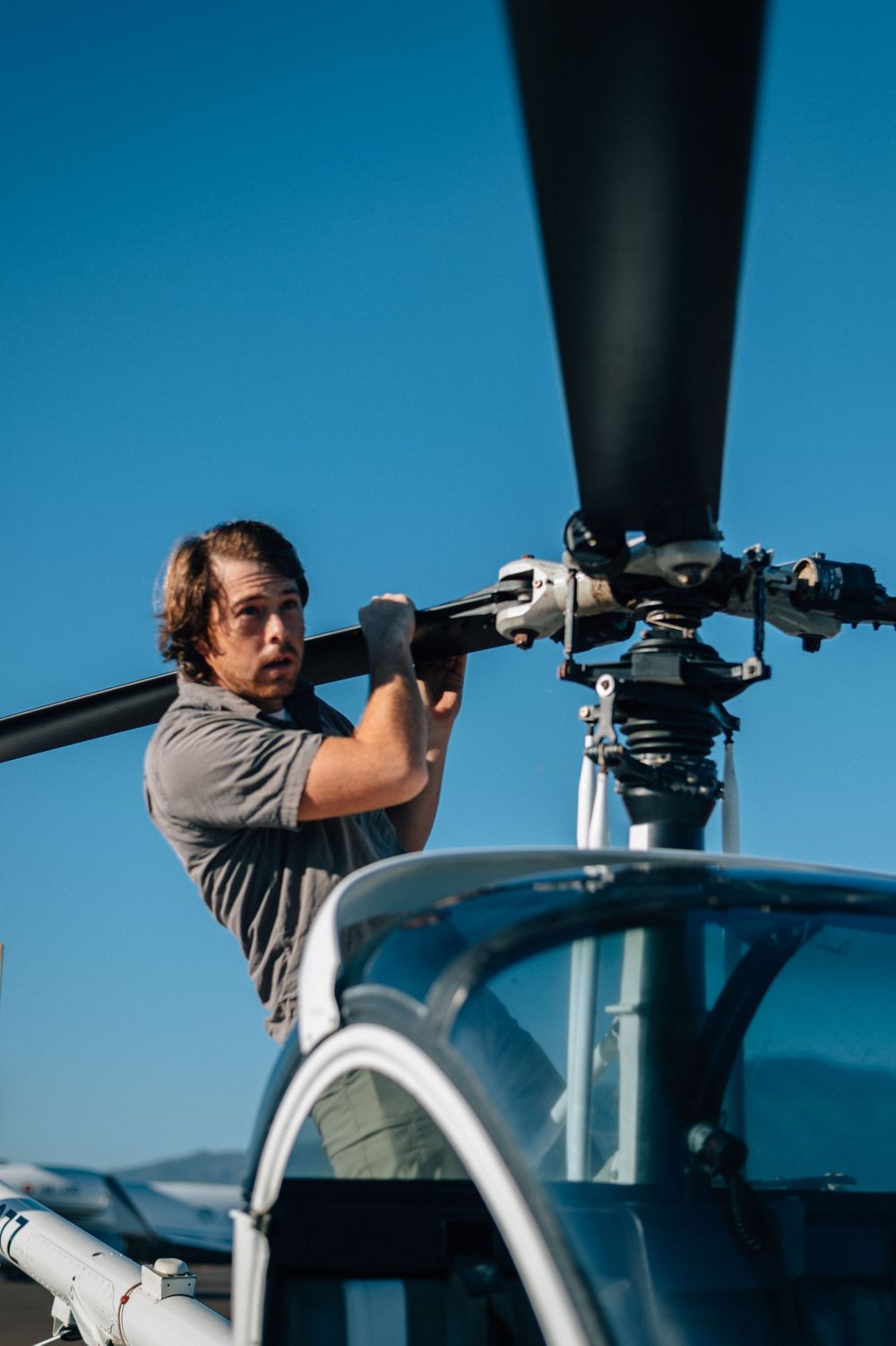 Person examining helicopter rotor blades during pre-flight inspection.