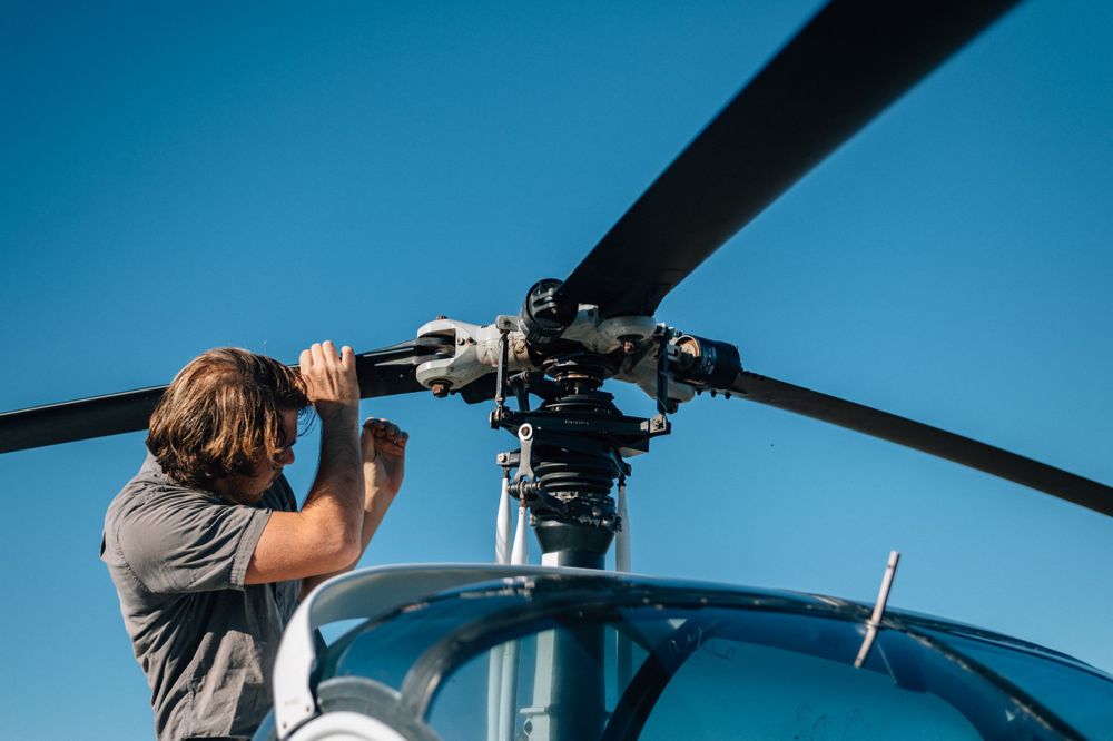 Detailed inspection of helicopter rotor system against clear blue sky.