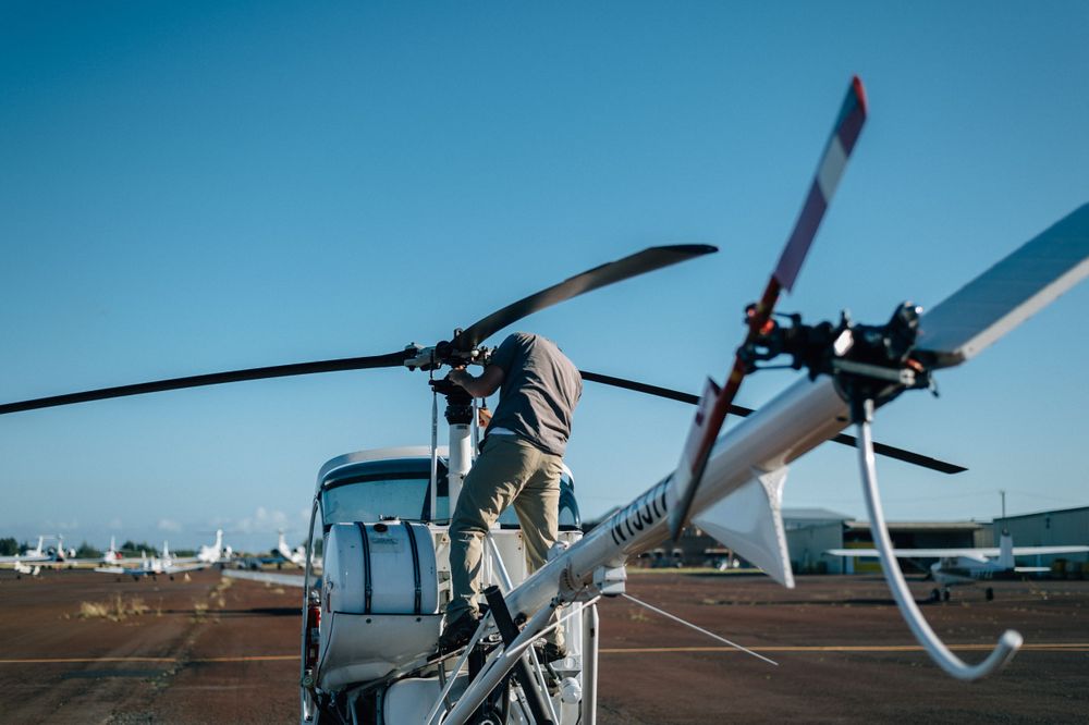 Helicopter maintenance inspection being performed on tarmac with other aircraft visible.