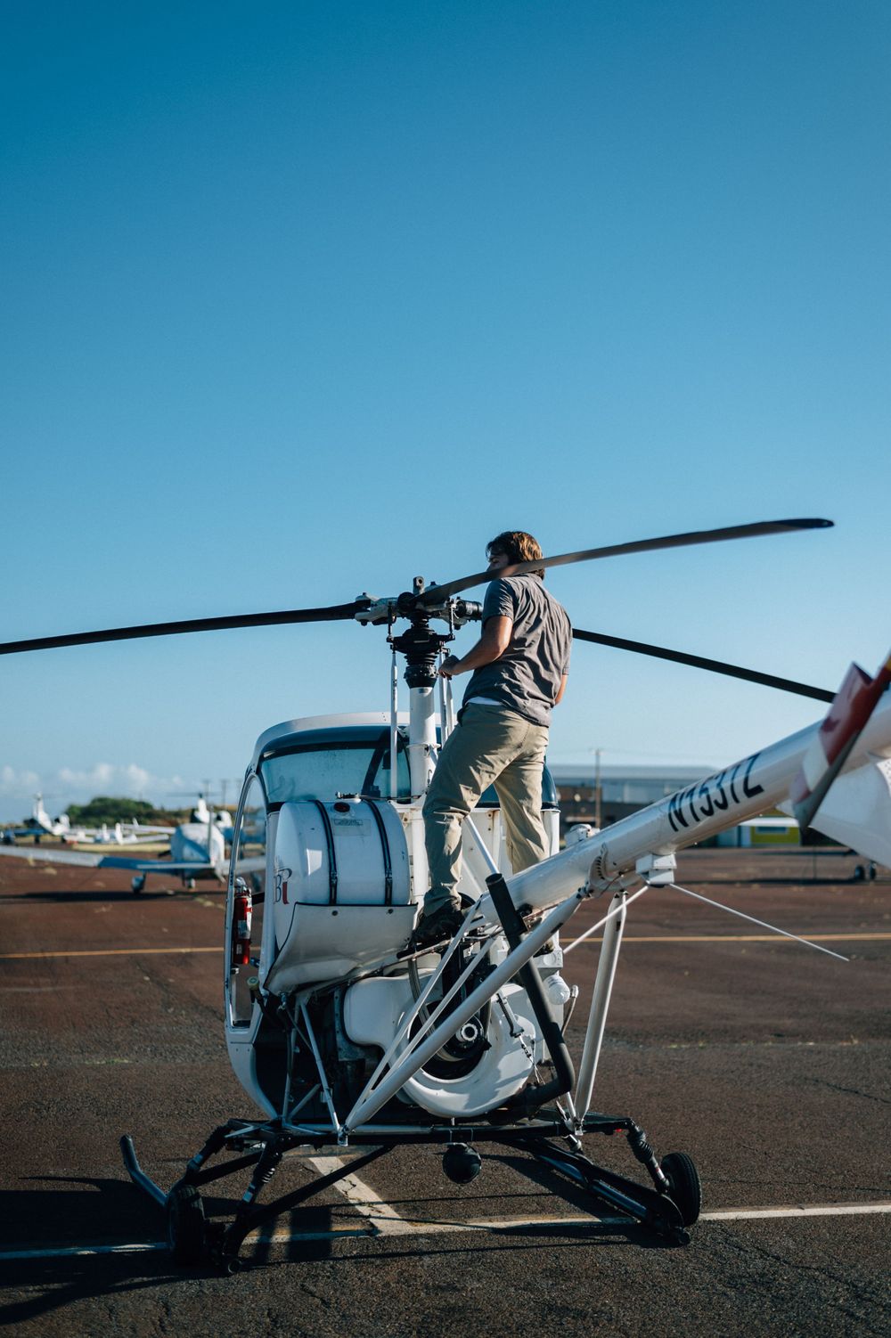 Ground crew member performing detailed rotor blade inspection on parked helicopter.