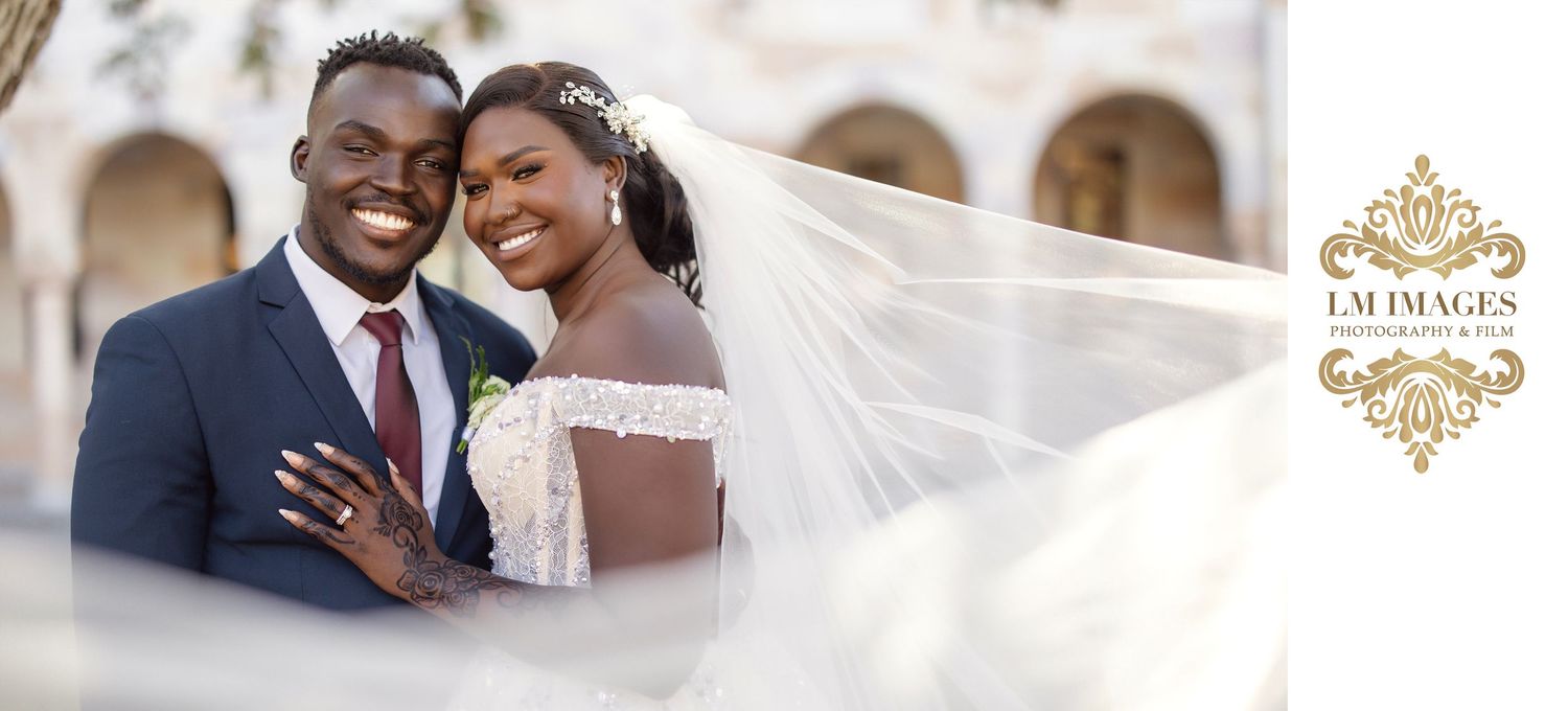 African American bride and groom pose outdoors with flowing veil under the EM Images logo.