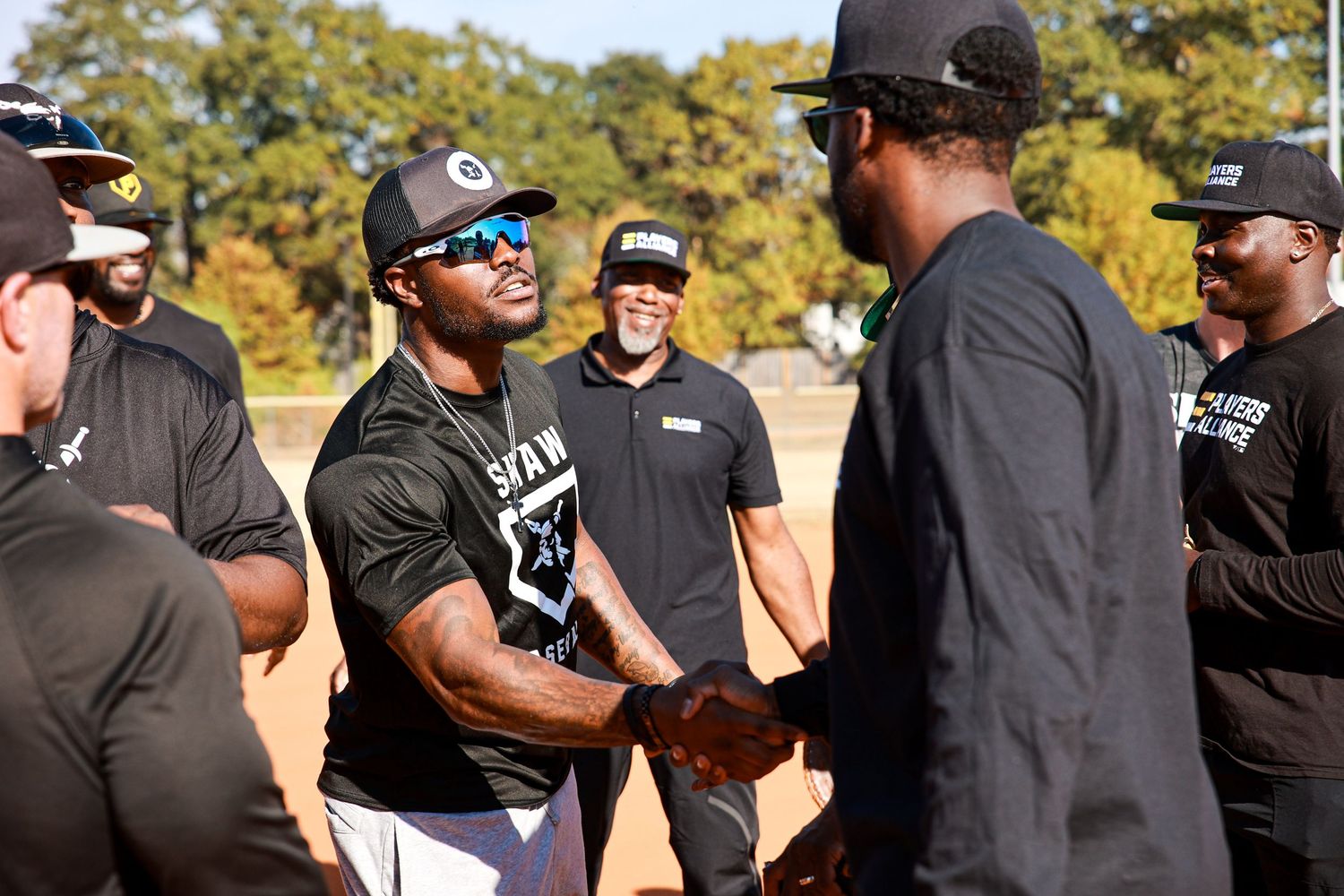 A group of people wearing black t-shirts and hats gather outdoors in bright sunlight.